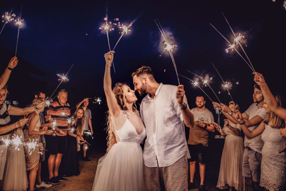 a happy couple kissing at their wedding ceremony with guests holding sparklers